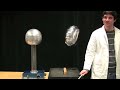 First, a dipole consisting of two conducting balls connected by an insulating rod swings at the end of a long plexiglass rod. The two balls are charged oppositely by touching it to a conducting rod in the field of a Van de Graaff generator. The generator is negatively charged, which induces a positive charge on the closer silver ball, and a negative charge on the further gray ball. Going around the generator, the dipole always aligns itself with the electric field, ie the silver ball always ...