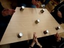Four young people are performing a rhythm, which is produced by body percussion and paper cups.