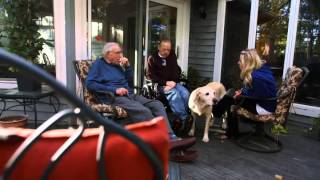 three people sitting on porch with a dog