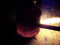 this is a basic waste oil burner.  we made this from an old a/c freon bottle we had laying around the house.  we then cut two holes into it, welded a pipe on the upper most hole and use it as the air inlet.  the bottom hole was left open as the exhaust.  

for the fuel, we took a half inch steel pipe and threaded it into the bottom backside of the bottle.  if you look closely in the video you can see it.  the fuel is any type of waste oil, peanut oil in this case.  we have the fuel in a rubbing alcohol bottle, which is connected to a ball valve, which is connected to the steel pipe on the bottom.

the burner is a bit complicated to get started because you need very high heat to start the oil fire.  the oil will only burn if it is hot enough to vaporize the oil.  to get it started we had to light some charcoal on the side and then place them into the bottle once they are glowing hot.  we then force the air in via an old vacuum that we rigged to blow air.  as the coals glow brighter, we slowly introduce the oil which starts to burn if it is hot enough.  the hotter the bottle gets, the better the oil burns.