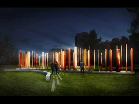 Visitors approach clusters of slender bronze columns illuminated at night.