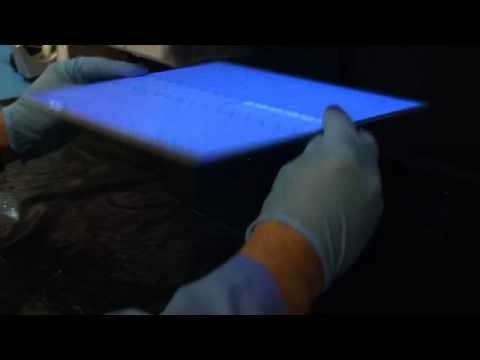 UV conformal coating - An operator inspecting a printed circuit board after a conformal coating process under a UV light in an inspection booth after de-masking, re-work and finish...