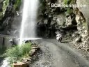 A waterfall falling on the road and Varun crossing it on his motorcycle.