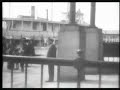 depicts scenes at the immigration depot and a nearby dock on ellis island. appears to show, first, a group of immigrants lined up to board a vessel leaving the island, then another group arriving at the island and being directed off of the dock and into the depot by a uniformed official.