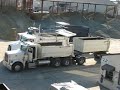 13 DECEMBRE 2007 .CAMIONS-REMORQUES EN DECHARGEMENT DE GRAVIER .A NOTER LA 2EME BENNE AMOVIBLE NOMMEE EN ANGLAIS LA B-BOX (BOITE B), SYSTEME TRES COURANT AUX USA , QUI VIENT S' EMBOITER DANS CELLE DU PORTEUR , ET EGALEMENT LES PORTEURS TELECOMMANDES DEPUIS L' ARRIERE POUR FACILITER L' ACCROCHAGE DE LA FLECHE QUAND LE CONDUCTEUR EST SORTI DE LA CABINE POUR DEVERROUILLER LES PORTES ARRIERE AINSI QUE LES LOQUETS DE FIXATION DE LA 2EME BENNE .POUR FAIRE PASSER LA BENNE DE LA REMORQUE AU PORTEUR , LES 2 CHASSIS DOIVENT VENIR S' ENCASTRER L' UN DANS L' AUTRE PAR 2 ENCOCHES JUSTE SOUS LA 1ERE BENNE (CELLE DU PORTEUR) , CE QUI EXPLIQUE QUE LE CHAUFFEUR DOIT RECULER JUSQU' A CE QUE LES 2 VEHICULES SOIENT EN CONTACT .CE SYSTEME DE CAMION REMORQUE PERMET D' EVITER L' ENSEMBLE SEMI REMORQUE BENNE ET LIMITE LE NOMBRE DE MANOEUVRES AVANT BENNAGE .IL PERMET AUSSI D' EVITER DES CIRCUITS HYDRAULIQUES COMPLEXES , DONC DU POIDS SUPERFLU .