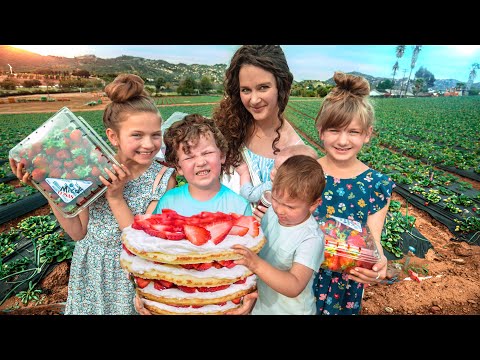 A woman with children in a strawberry field, proudly holding a large strawberry-topped layered cake.