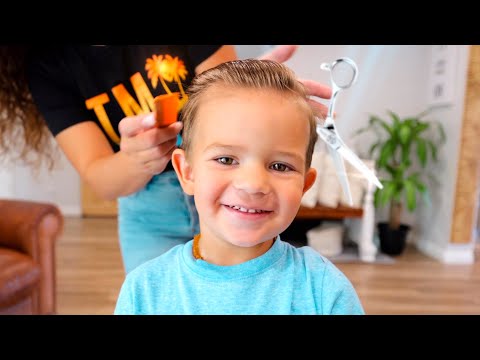 Smiling young boy having his hair styled by a person behind him in a home salon setting.