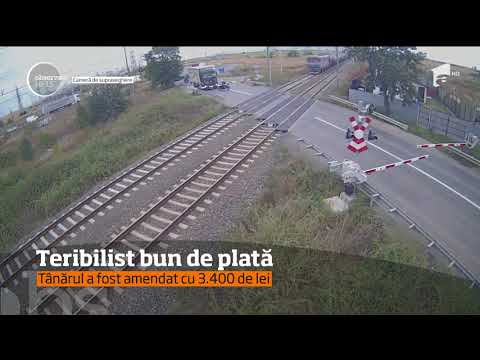 Un motociclist înaintează printre maşinile oprite în faţa barierei de la calea ferată și îi