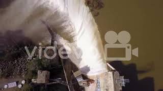 Beautiful rising aerial over a man standing beside high waterfall or dam in full flood stage near Oj