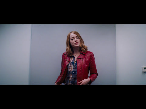 Trailer still: Mia in a single spotlight mid-audition, the camera circling as the orchestra swells