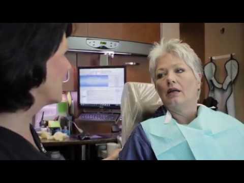 Woman in dental chair talking to dental team member