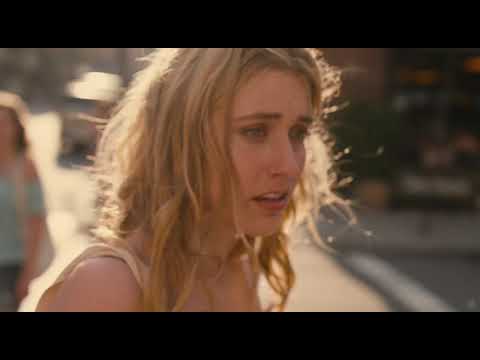 Trailer frame: Lola half-smiling under streetlights, earbud wire visible, city noise blurring behind her