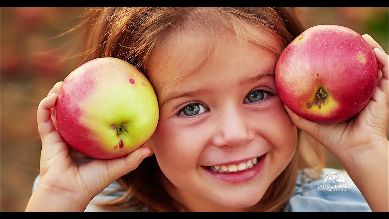 Smiling child holding two red apples beside their face