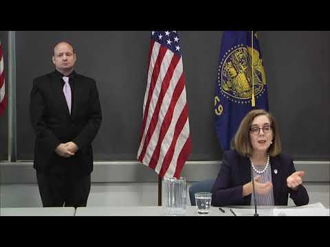 Governor Kate Brown holding a mask with one sign language interpreter standing behind her.