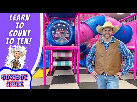 Man in a cowboy hat and vest posing in a colorful indoor playground, with a purple banner that reads 'Learn to Count to Ten!' on the left.