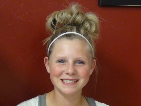 Girl smiling with a high messy bun hairstyle secured by a headband, showcasing practicality and style for active days.