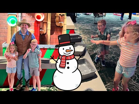 Man in a cowboy hat pose with three children at a colorful indoor play area; cartoon snowman overlays the foreground.