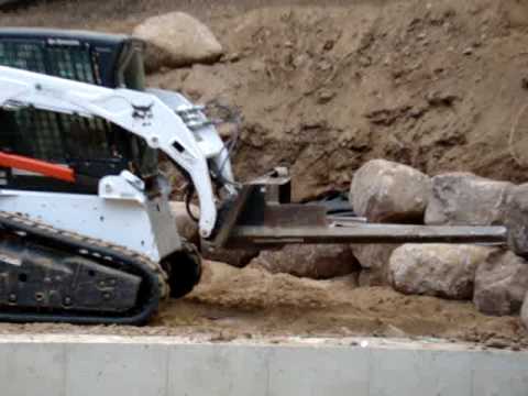 Boulder rock wall building with a bobcat and hydraulic forks.