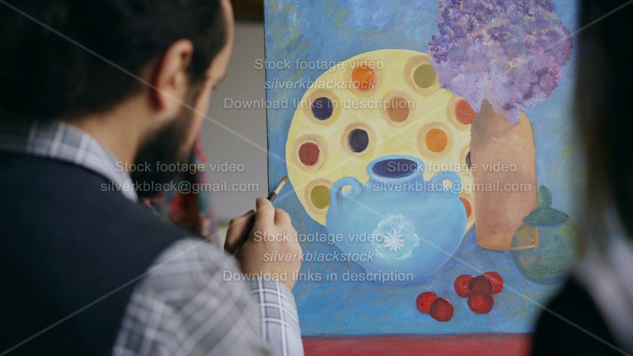 Close-up of Skilled artist man teaching and showing young girl the basics of painting in art studio