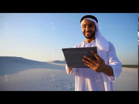Successful Arabian businessman holds in hands and uses tablet, standing among big desert on summer