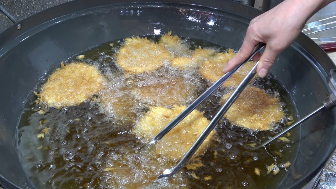 A Korean cheese donkkaseu pork cutlet pulled apart with mozzarella cheese stretching out from the breaded cutlet on a Korean street food plate
