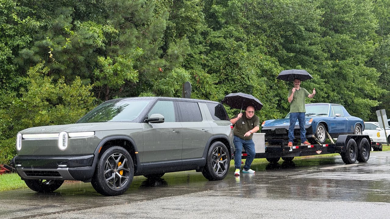 Rivian R2 electric SUV towing a car hauler trailer in the rain