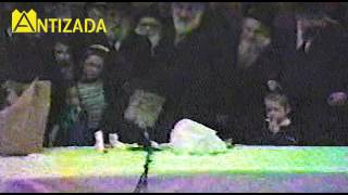 הרבי מליובאוויטש מעיר (בעדינות) ילד שנרדם ליד רגליו בהתוועדות פורים תשמ"ג - התמונה מוצגת ישירות מתוך אתר האינטרנט יוטיוב. זכויות היוצרים בתמונה שייכות ליוצרה. קישור קרדיט למקור התוכן נמצא בתוך דף הסרטון