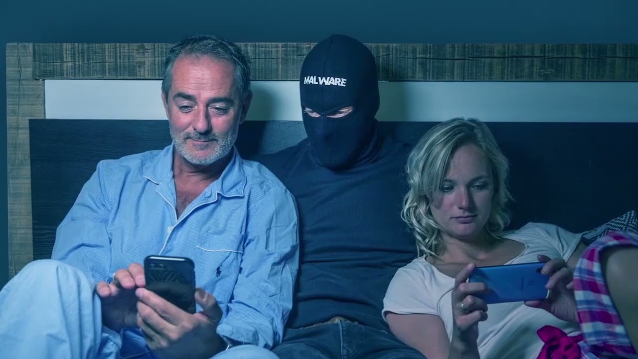 Een stel in bed, met tussen hen in een persoon met een bivakmuts.