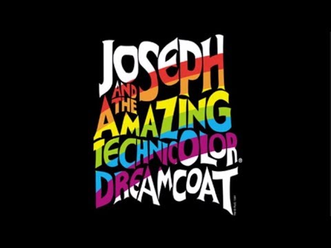Technicolor coat close-up beneath stage lights; brass and children’s chorus implied