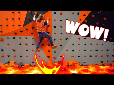 Climber in a safety vest scales an indoor orange-gray climbing wall, with a fiery lava graphic at the bottom and a big WOW! caption overlay.