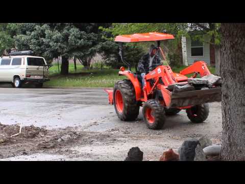 Kubota Tractor moving a bunch of cement from a torn up driveway in the rain