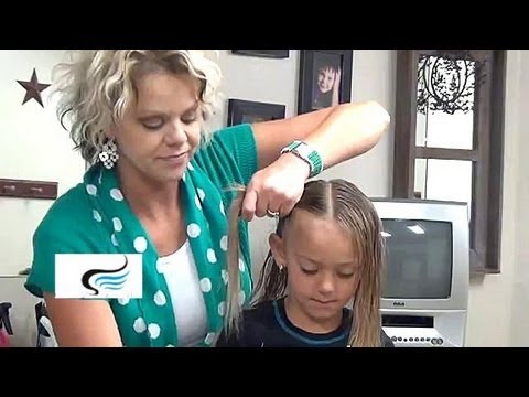Woman styling a little girl's hair, demonstrating a pigtail hairstyle tutorial, in a home setting with a television in the background.