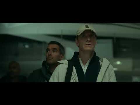 The Killer (2023) official trailer frame: Michael Fassbender’s assassin behind tinted glasses, city blur outside