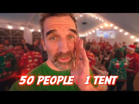 Bearded man in a green shirt in a festive tent with string lights and people in Christmas sweaters; overlay text reads '50 PEOPLE 1 TENT'