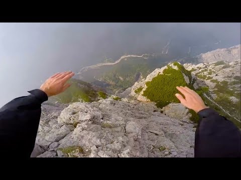 BASE jumper flies along the side of a cliff.