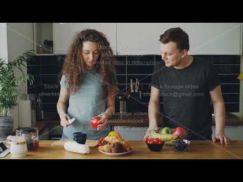 young caucasian loving couple kissing and putting different vegetables and fruits on table to cut