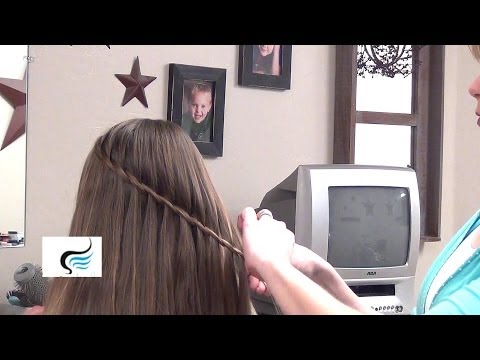 Person demonstrating a twist hairstyle on medium-long hair, showcasing a simple twist technique suitable for busy mornings, with a backdrop of a home setting and framed photos.