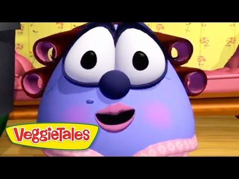Blue, chubby VeggieTales character with large eyes, pink lips, and rosy cheeks smiles in a colorful room; VeggieTales logo bottom-left.