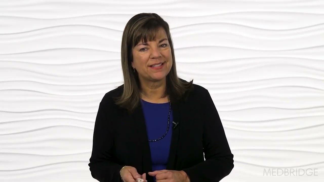 A woman with straight brown hair in a black blazer stands smiling with a marker before a white background, with the medbridge logo in the corner.