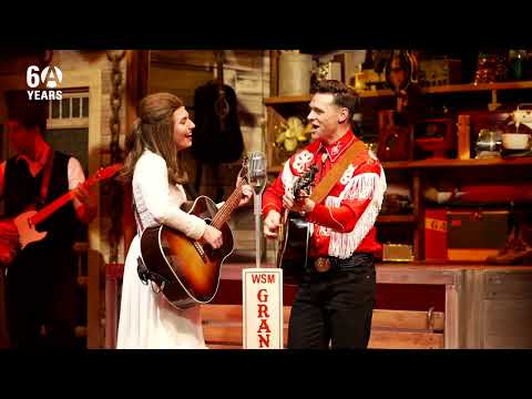 Trailer still showing guitars, banjo, fiddle and a semicircle of singers under warm lighting