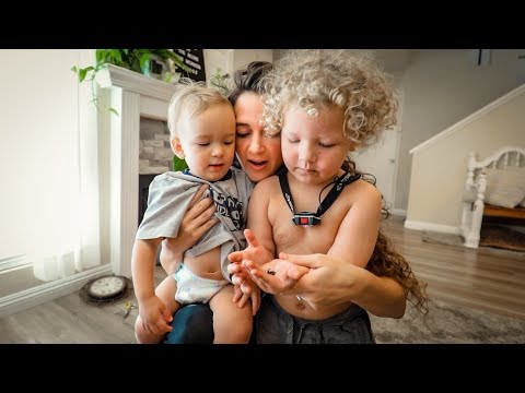 Mother holding two toddlers close as they examine something in her hands in a bright living room.