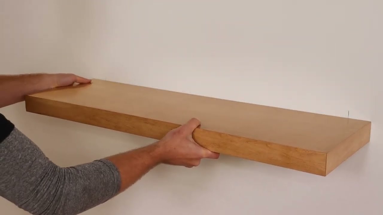 Hands setting a wood floating shelf onto a wall-mounted EZ-LOC bracket