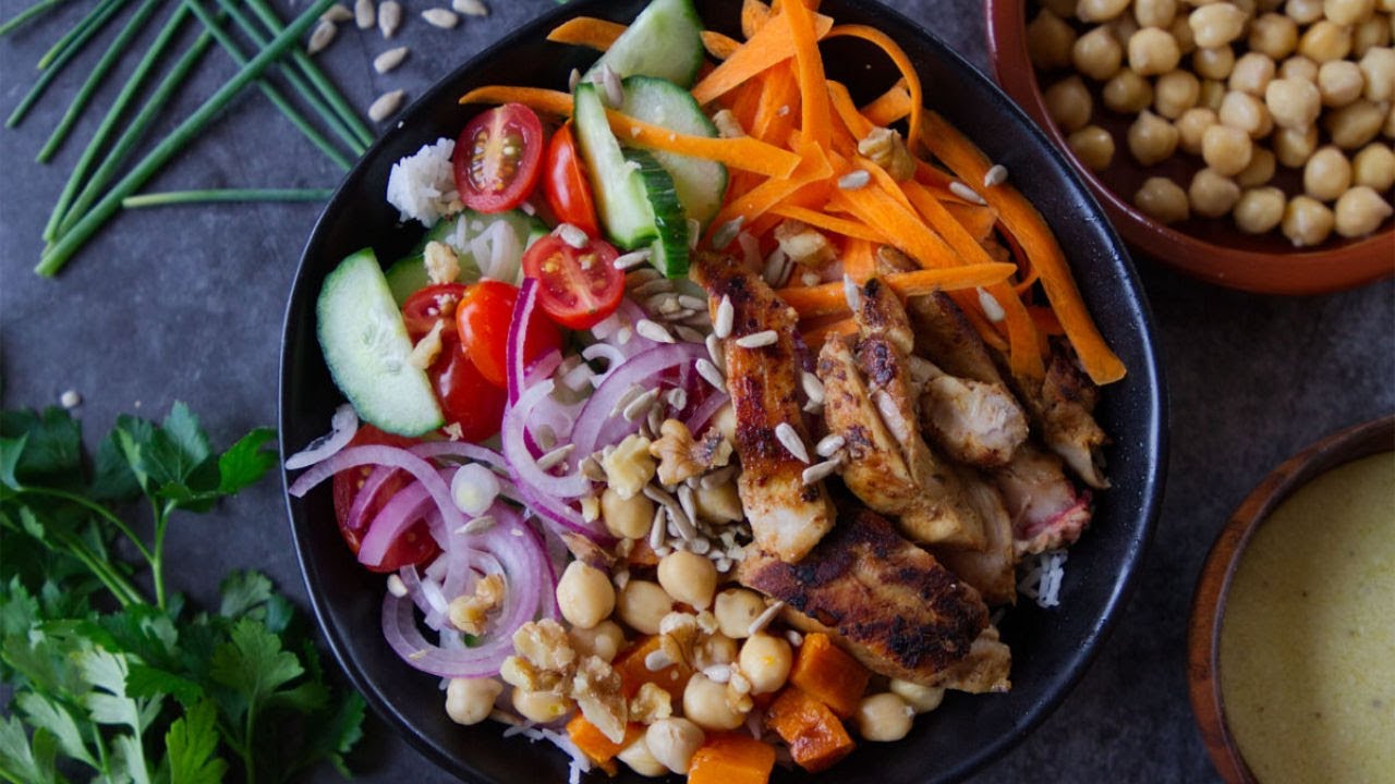 A grilled chicken and salad rice bowl with some seeds and garnishing