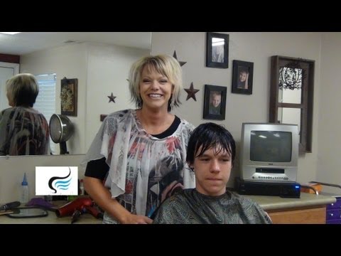 Hair stylist with short blonde hair smiling beside a young boy in a salon chair, preparing to bleach boys' hair for a trendy look, highlighting accessible hairstyling techniques.