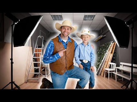 Man and boy in cowboy outfits posing in a photography studio with lights and props nearby.
