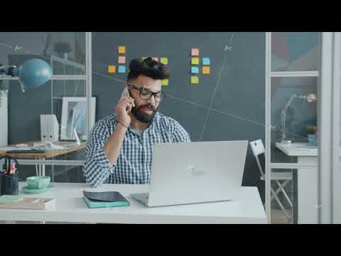 Arab businessman in casual clothing and glasses talking on mobile phone and using laptop at work