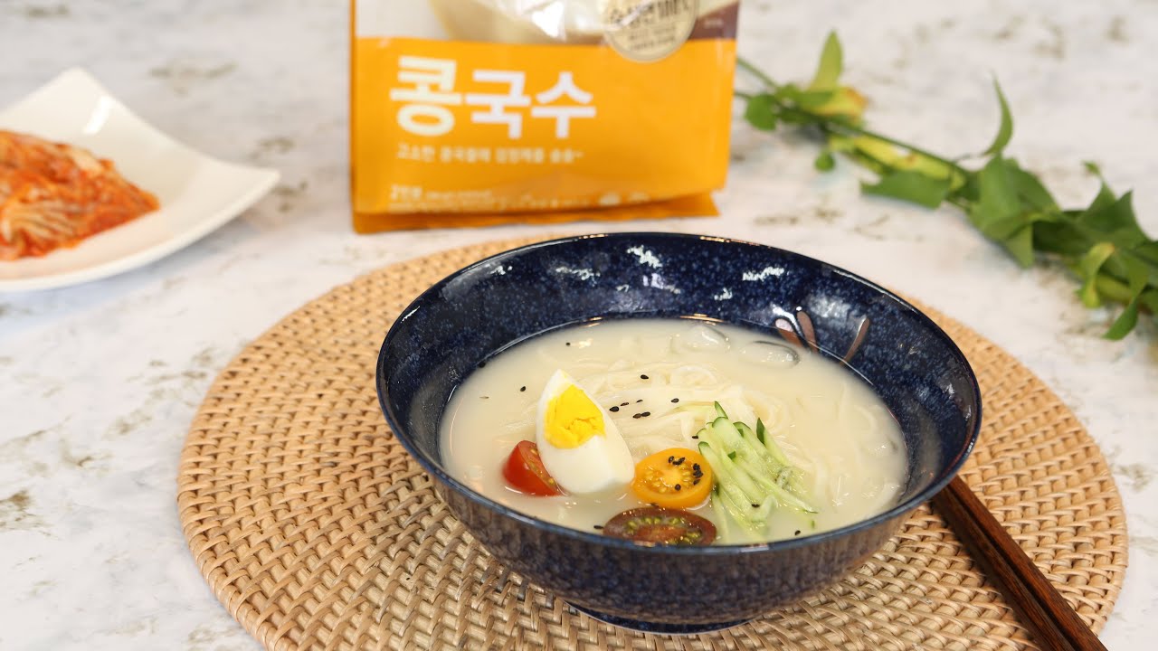 A large bowl of Korean kongguksu cold soybean noodle soup with white creamy broth thin wheat noodles cucumber slices and sesame seeds on top