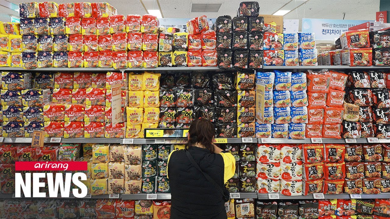 A shopper in front of supermarket shelves stacked with packs of Korean instant noodles