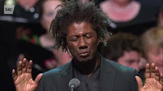 Christopher Tin conduzindo &quot;Baba Yetu&quot; ( Pai Nosso em Suaíli ) ao vivo em Llangollen.