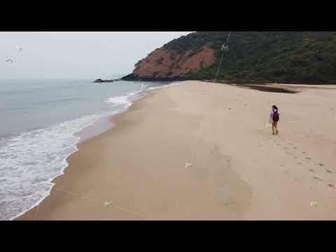 a girl with a backpack walks along a deserted wild beach by the sea aerial shot